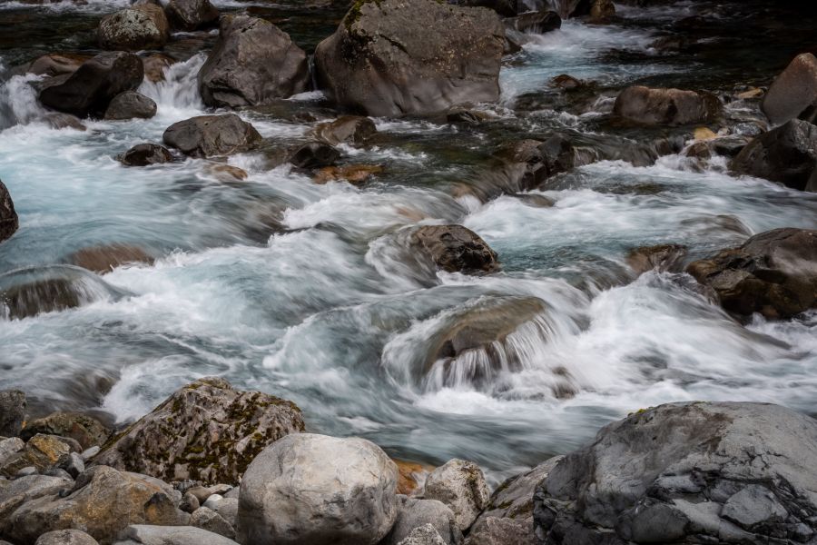 Rushing river water flows over large rocks and boulders, creating white rapids.